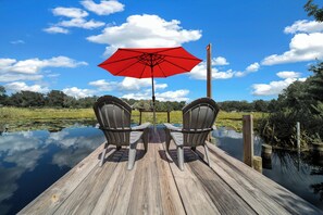 A wooden dock with two chairs and a red umbrella.