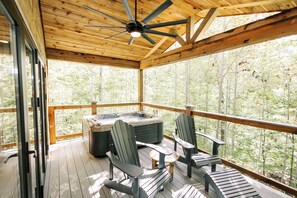 A wooden deck with a hot tub, two Adirondack chairs, and a ceiling fan. - New Adults-Only Cabin | Hot Tub, Sauna, Plunge (Zachariah)