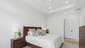 A bedroom with a wooden bed, bedside tables, a nightstand, a lamp, and a plant. - New Build Modern 3BR HTX Home • King Beds • Parking • Pet Friendly (Houston)