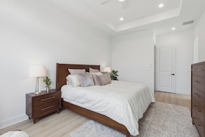 A bedroom with a wooden bed, bedside tables, a nightstand, a lamp, and a plant. - New Build Modern 3BR HTX Home • King Beds • Parking • Pet Friendly (Houston)