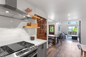 A modern kitchen with a gas stove, wooden shelves, and a view into a dining area with a table and chairs. - Lakeside Cavern | Lake Views | 3 Decks | Sleeps 8 (Lake Arrowhead)