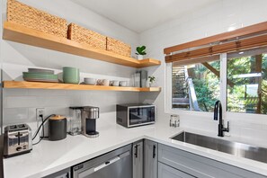 A modern kitchen with built-in appliances, wooden shelves, and a window with a view of greenery. - Lakeside Cavern | Lake Views | 3 Decks | Sleeps 8 (Lake Arrowhead)