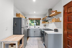 Eine kompakte Küche mit grauen Schränken, einem schwarzen Kühlschrank, einem Holztisch und einem Fenster mit Blick ins Grüne.