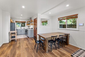 A compact kitchen with modern appliances, a dining area with a wooden table and chairs, and a window with a view of greenery. - Lakeside Cavern | Lake Views | 3 Decks | Sleeps 8 (Lake Arrowhead)
