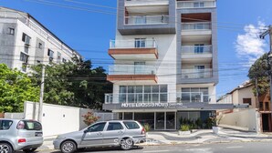 Un hotel de varios pisos con balcones, un letrero que dice "HOTEL BOSSA NOVA" y un estacionamiento con coches.