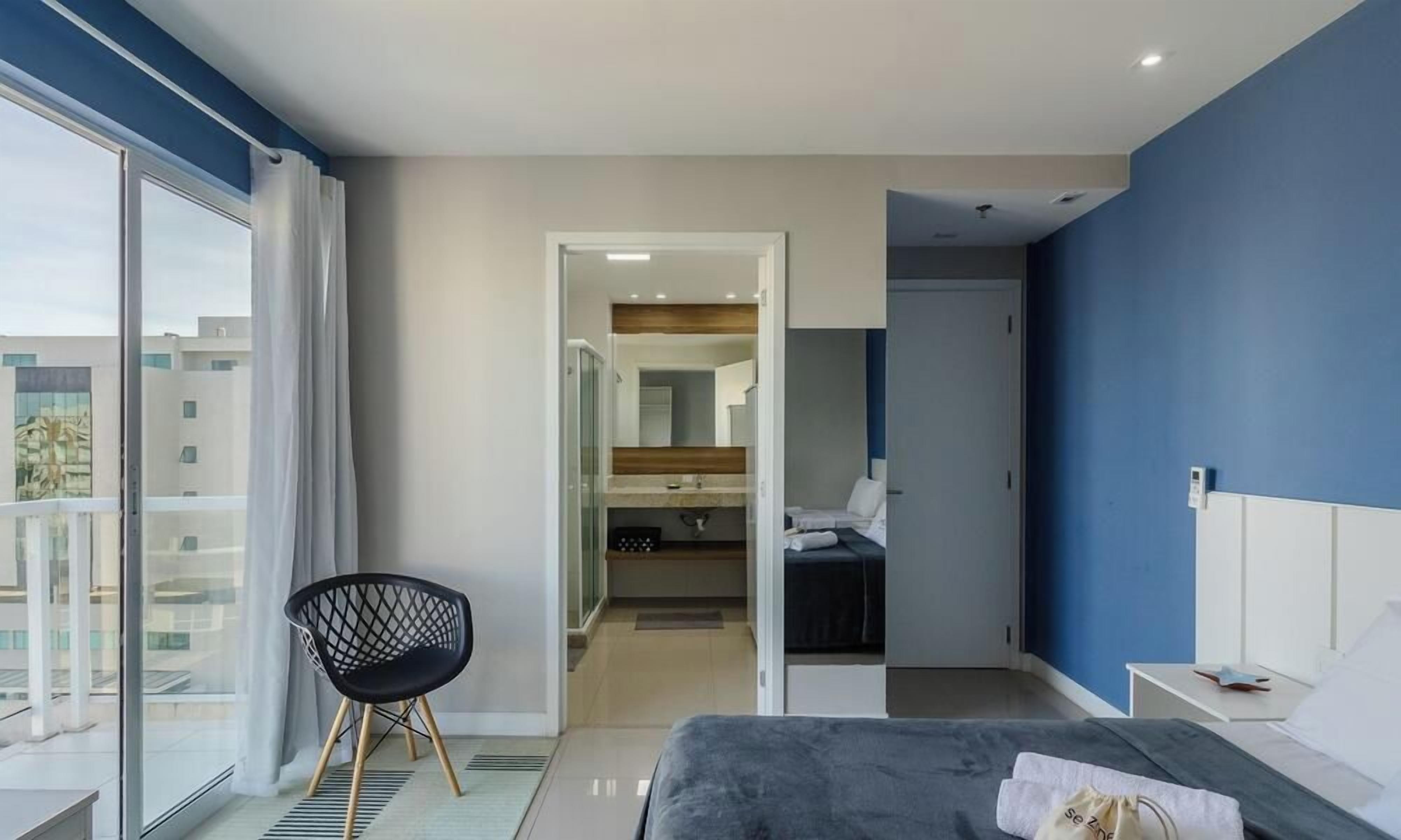 Moderni hotellihuone, jossa on sänky, tuoli, kylpyhuone ja suuri ikkuna, josta on näkymä.