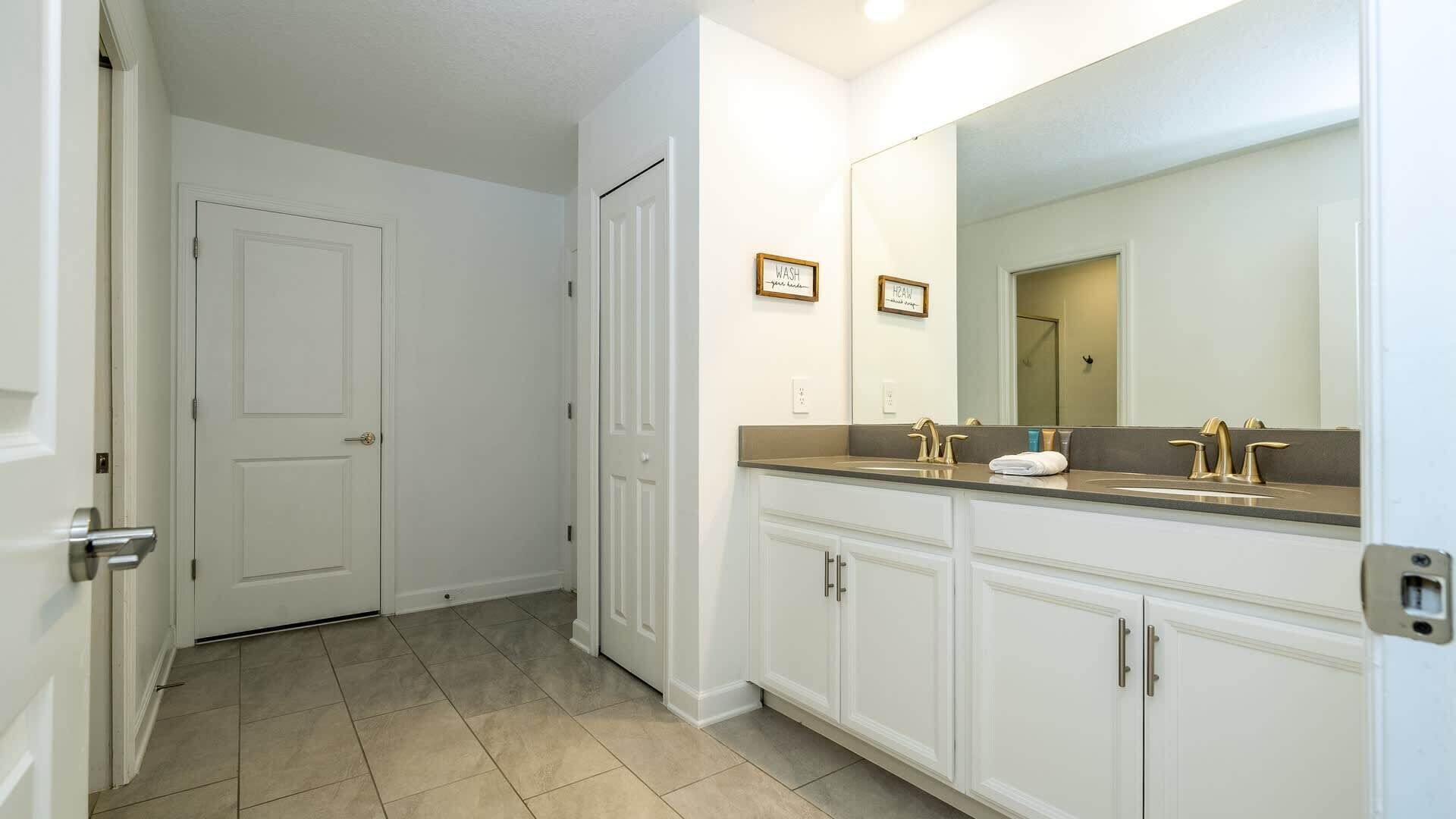 Un baño con lavamanos doble, un espejo grande y una puerta que da a otra habitación.