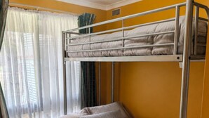 A bunk bed in a room with yellow walls, a window with sheer curtains, and a wooden chair.