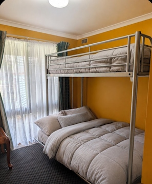 Un lit superposé dans une pièce aux murs jaunes, une fenêtre avec des rideaux légers et une chaise en bois.