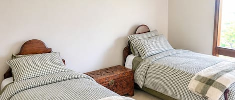 Un dormitorio con dos camas de madera, ropa de cama a cuadros, un pequeño cofre de madera y una lámpara en el techo.