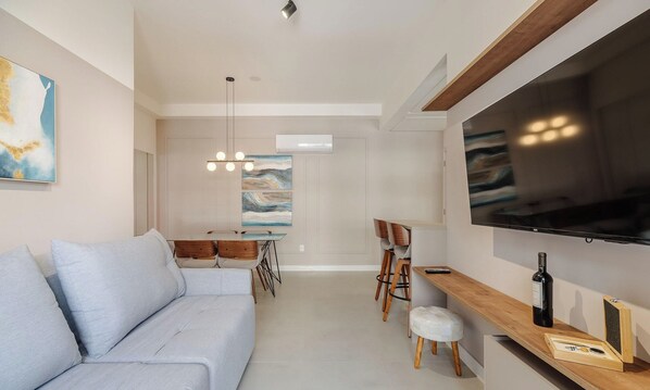 Una sala moderna con sofá, comedor y televisor montado en la pared.