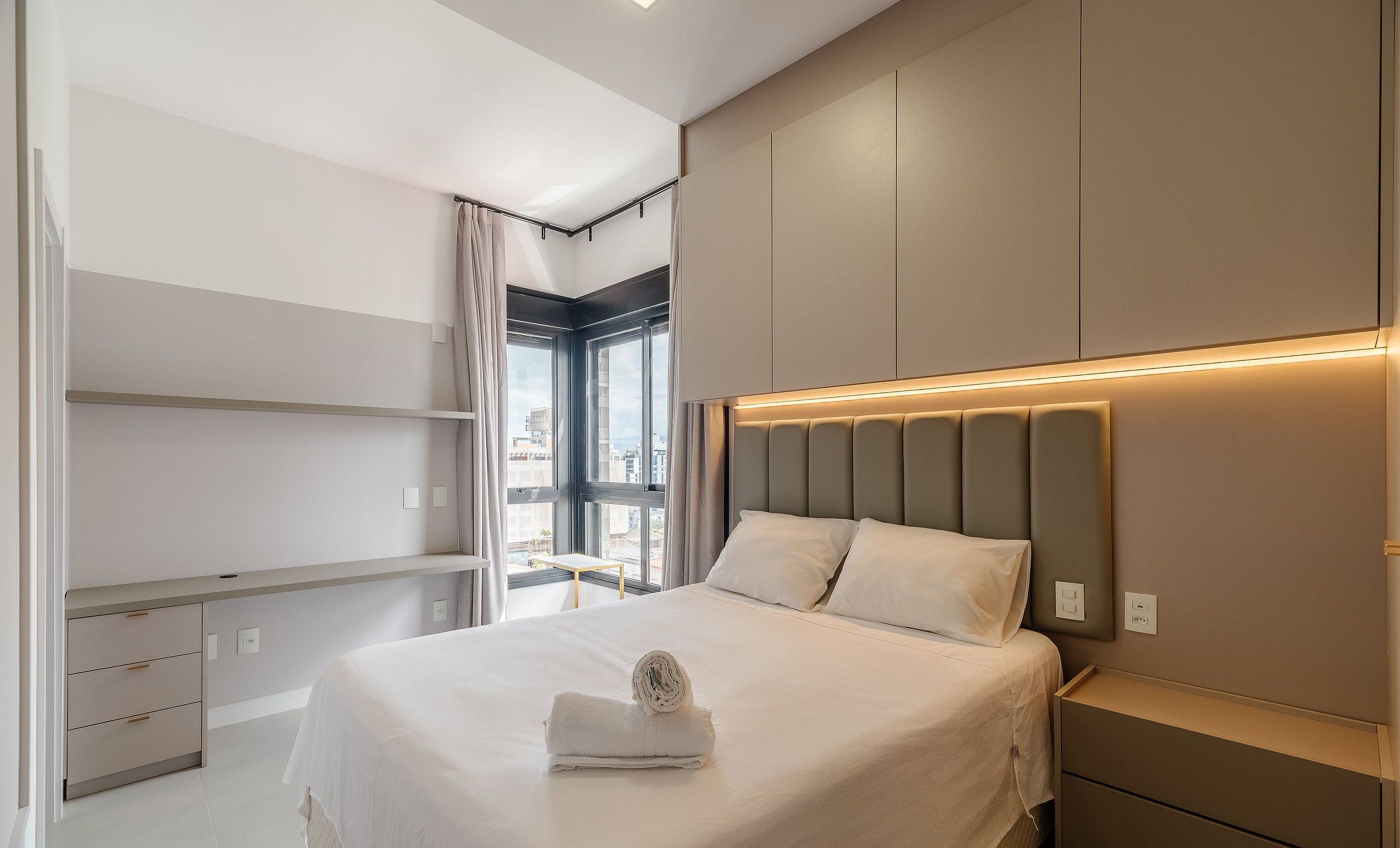 A modern hotel room with a large bed, built-in wardrobe, and a view of the city.