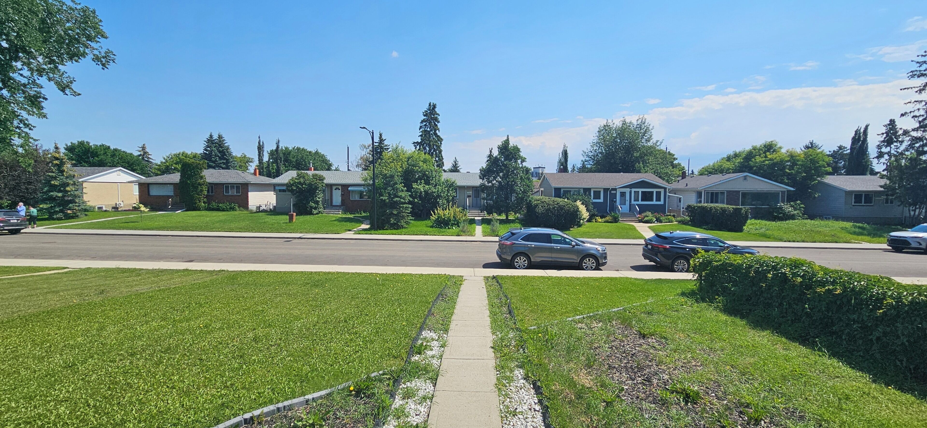 A suburban street with houses, cars, and a sidewalk.