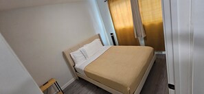 Ein Einzelbett mit Kopfteil, ein Nachttisch und ein Fenster mit Vorhängen.