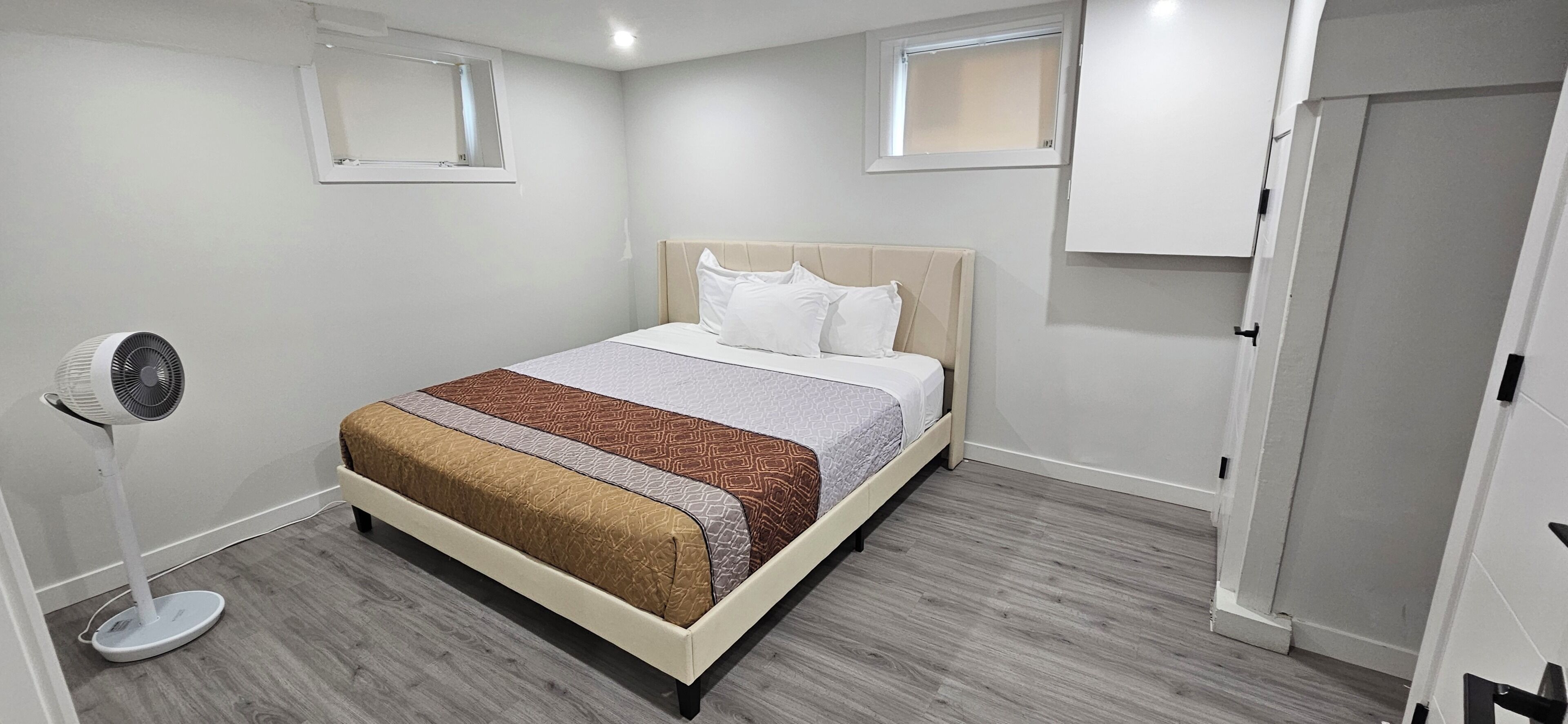 A hotel room with a bed, a standing fan, and a door.