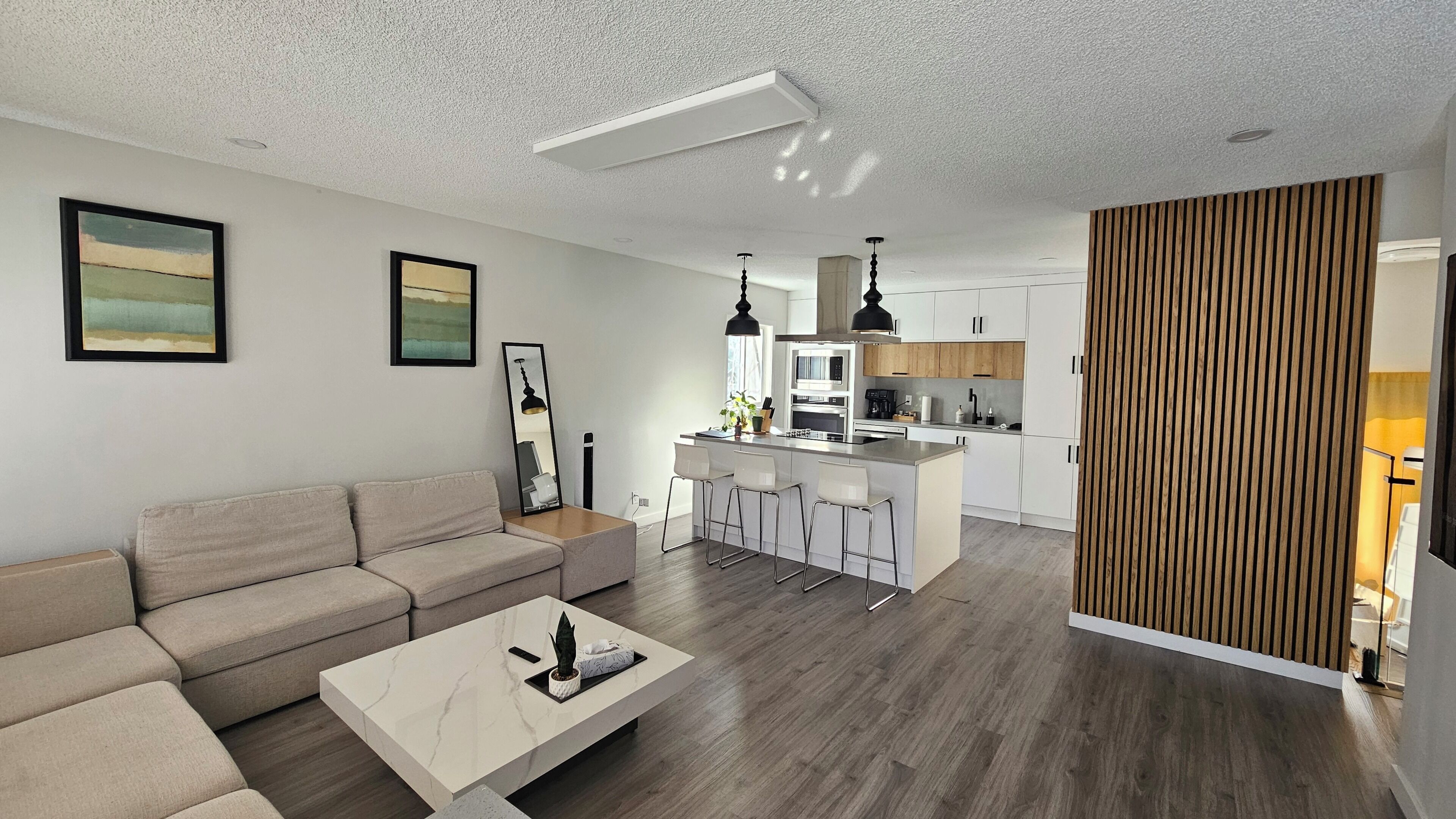 Un espacio habitable moderno con sofá, una mesa de centro, una cocina con isla central y un separador de madera.