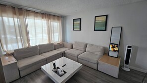 A modern living room with a sectional sofa, a coffee table, and a flat-screen TV. - Sarva Stays | Modern Avonmore Home | Sleeps 10 (Edmonton)