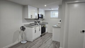 A modern kitchen with white cabinets, a built-in microwave, and a stainless steel stove. - Sarva Stays | Modern Avonmore Home | Sleeps 10 (Edmonton)