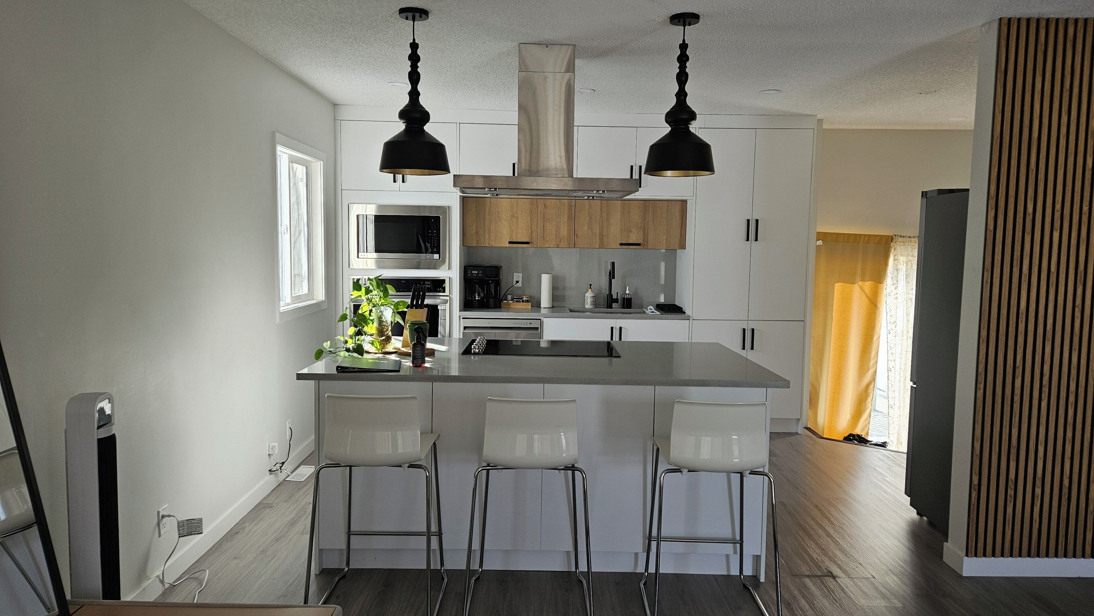 A modern kitchen with a central island, bar stools, pendant lights, and built-in appliances.