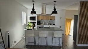 A modern kitchen with a central island, bar stools, pendant lights, and built-in appliances. - Sarva Stays | Modern Avonmore Home | Sleeps 10 (Edmonton)