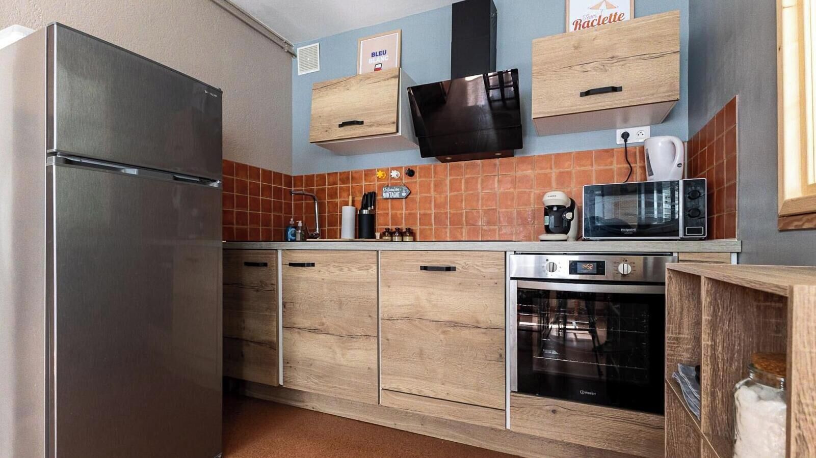 A compact kitchen with a stainless steel refrigerator, wooden cabinets, a microwave, and a coffee maker.
