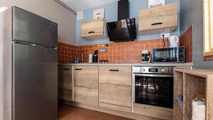 Una cuina compacta amb nevera d'acer inoxidable, armaris de fusta, microones i cafetera.