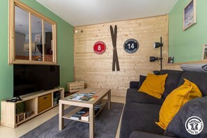 A living room with a television, wooden wall, skis, and a couch with yellow pillows. - The Val de Vendeix - LA BOURBOULE (LA BOURBOULE)