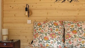 Habitació amb panells de fusta, un llit, roba de llit floral, una làmpada penjada a la paret i una obra d'art amb motius de muntanyes.