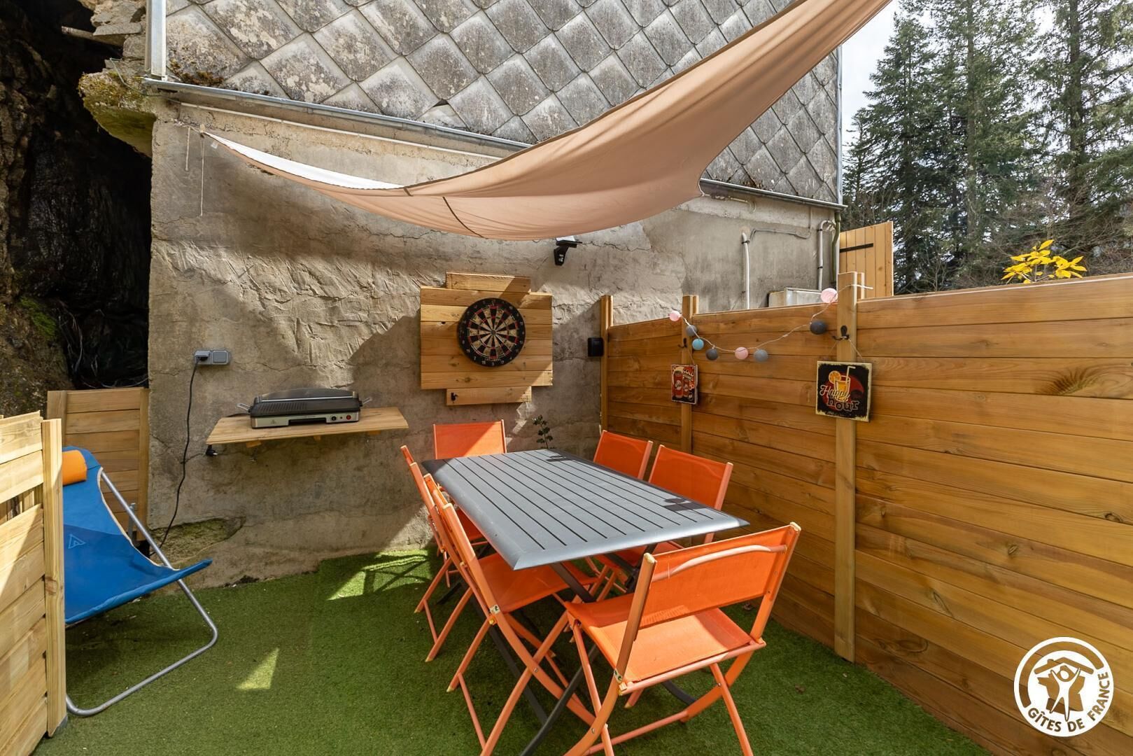 Une terrasse extérieure avec une table et des chaises, un jeu de fléchettes et une clôture en bois.