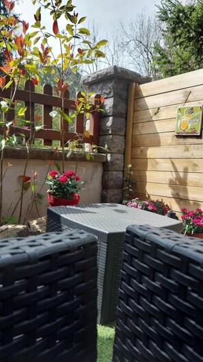 Eine Terrasse mit Tisch und Stühlen, ein Holzzaun und Kübelpflanzen.