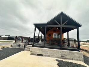 A wooden cabin with a covered patio, stone steps, and a metal railing. - Firefly Resort - Comfortably Uncorked #280 (Fredericksburg)