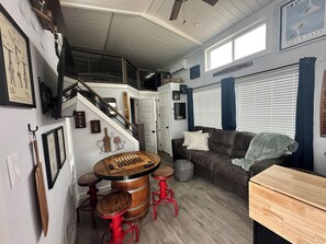Une pièce avec une table en bois, des tabourets rouges, un canapé en cuir marron et un escalier.