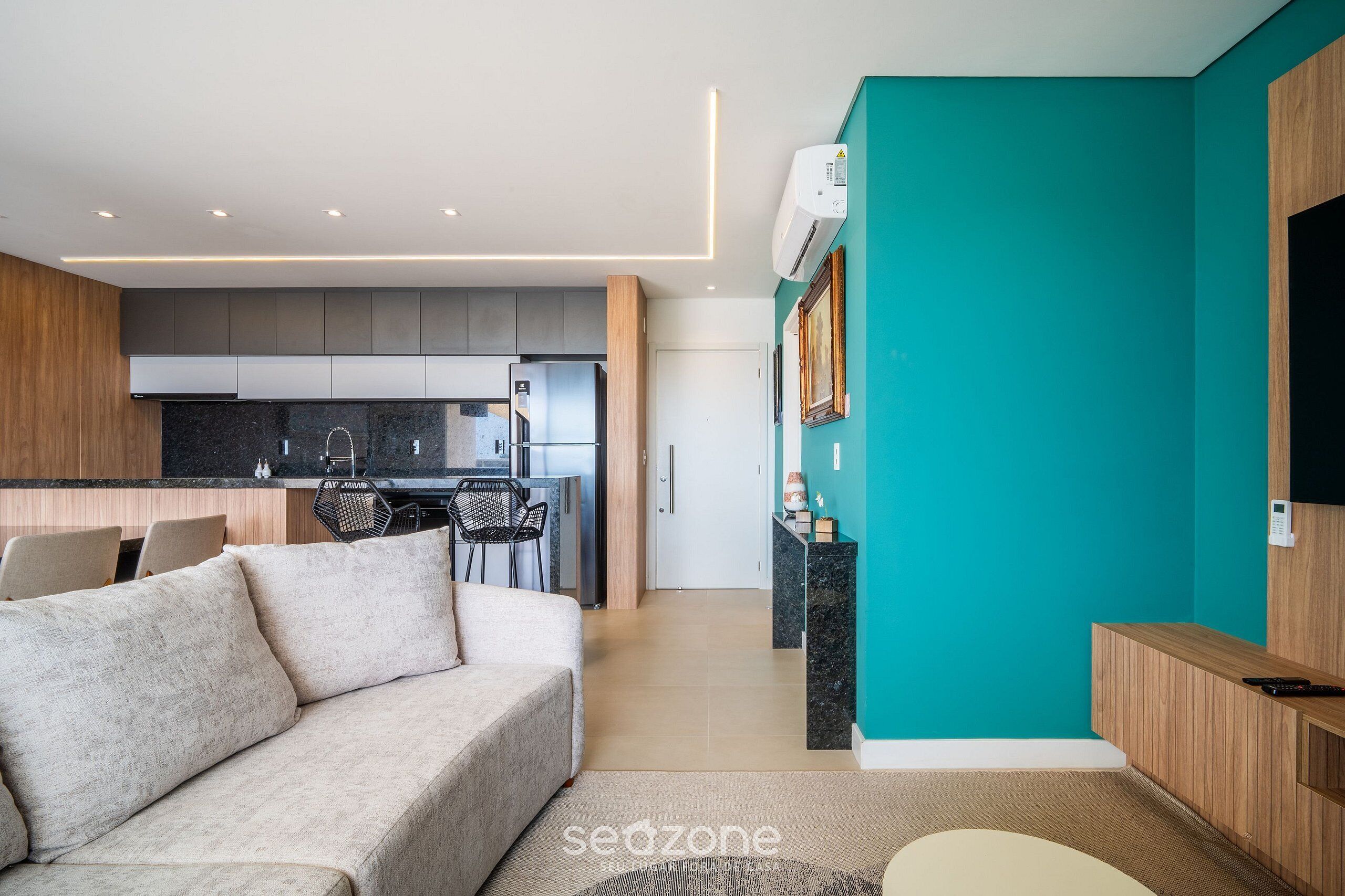 Una sala moderna con un sofá, un comedor con sillas, una cocina con armarios y una pared de acento color verde azulado.