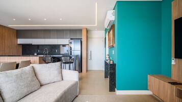 Una sala moderna con un sofá, un comedor con sillas, una cocina con armarios y una pared de acento color verde azulado.
