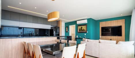 Una cocina moderna con una isla central, sillas de comedor, un sofá y un televisor de pantalla plana montado en la pared.