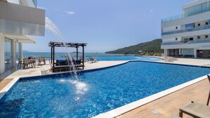 A swimming pool with a water feature, lounge chairs, and a view of the sea. - Penthouse With Ocean View Ingleses Mhc0306 (Florianópolis)