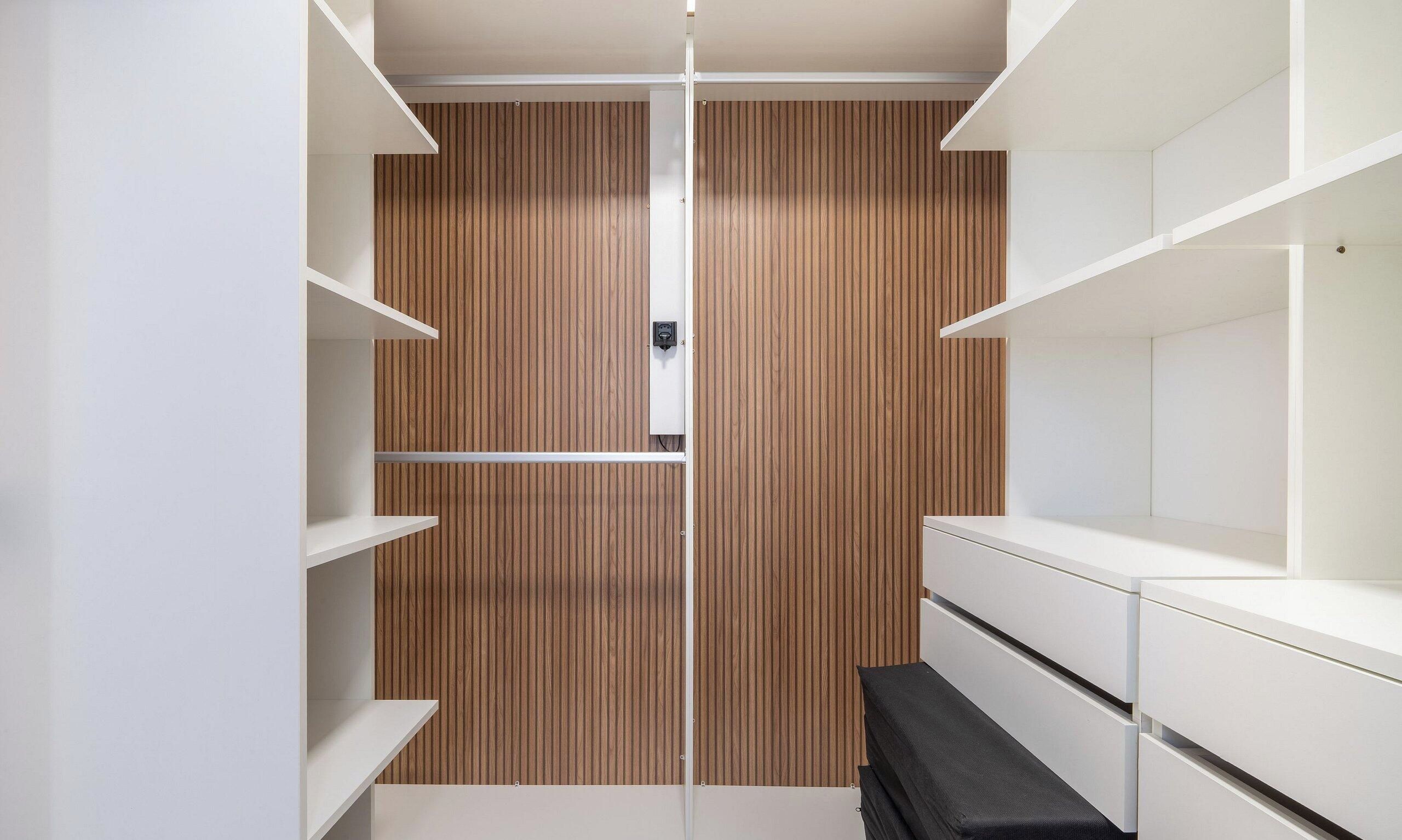 Un vestidor con paneles de madera, estanterías blancas y un banco.