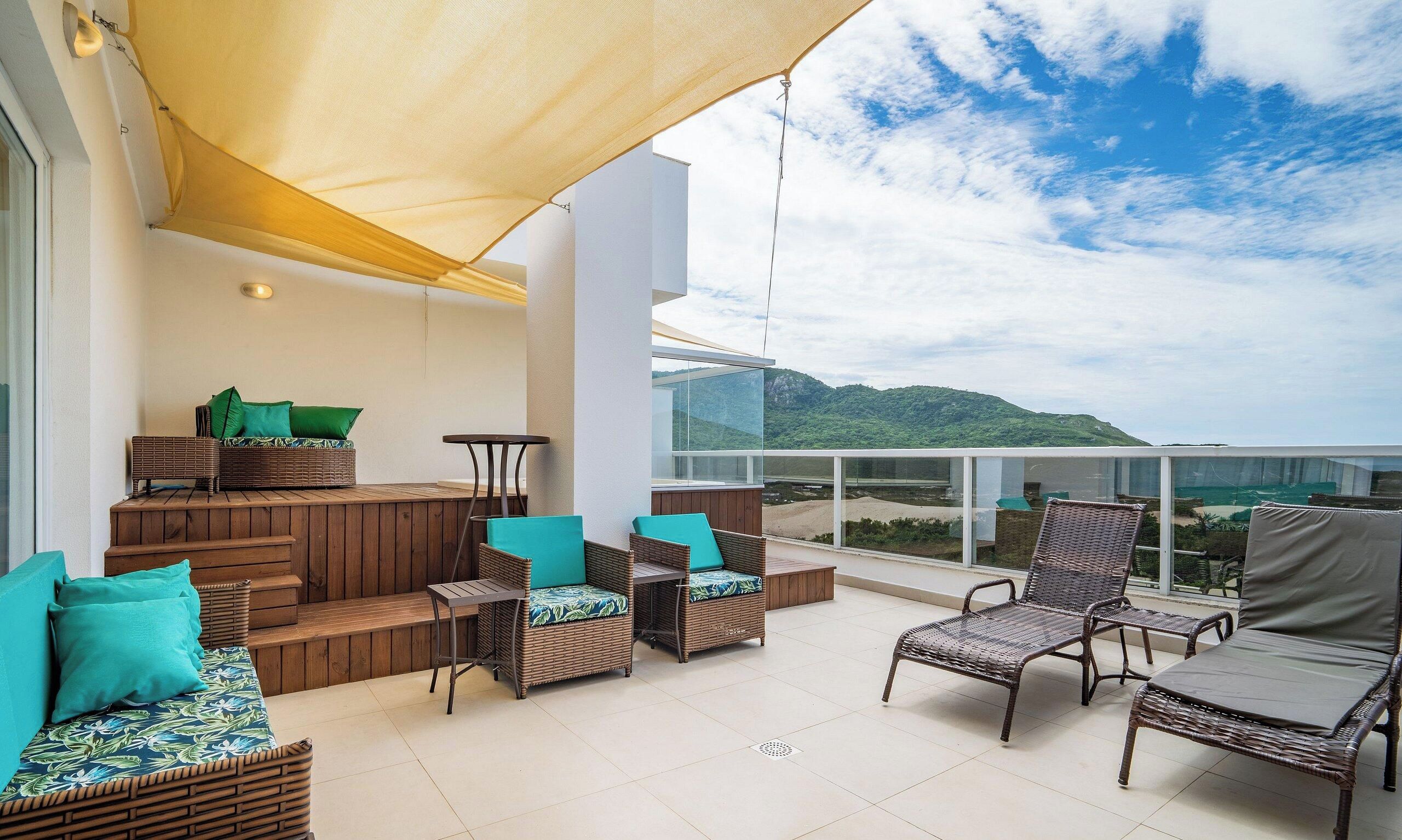 Un balcón con mobiliario de mimbre, un banco de madera y vistas a un paisaje montañoso.
