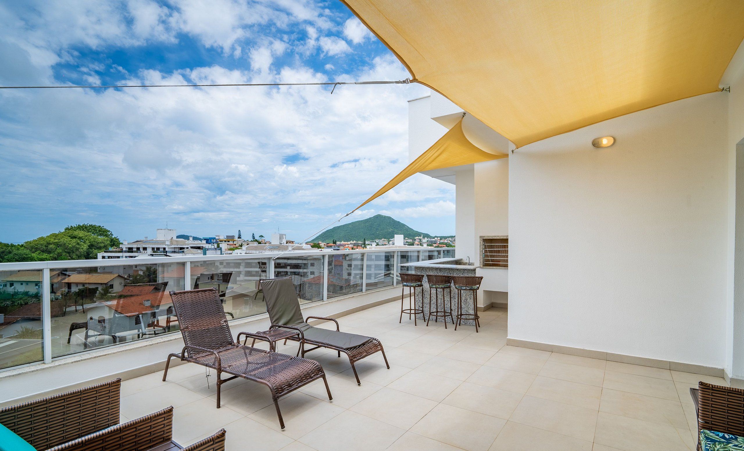 A rooftop terrace with wicker furniture, a bar area, and a view of a mountain and cityscape.