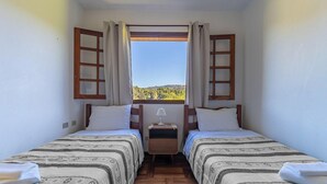 Una habitación pequeña con dos camas, una ventana con cortinas, una mesita de noche y vista a un paisaje.