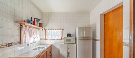 Cocina compacta con azulejos blancos, un mueble de madera, microondas y refrigerador.