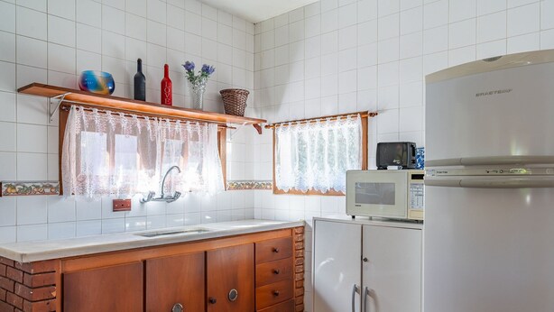 Una cocina con azulejos blancos, un mueble de madera, un microondas y un refrigerador.