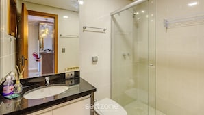 Un baño moderno con cabina de ducha de vidrio, tocador con lavamanos y espejo.