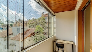 Un balcón con vistas a edificios y árboles, una mesita y una silla.