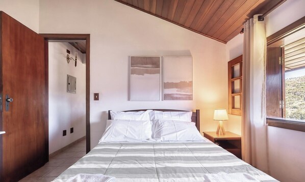 A bedroom with a bed, a nightstand, a lamp, and a window with a view. - Lovely House in Campos do Jordao Mcd001 (Campos do Jordão)