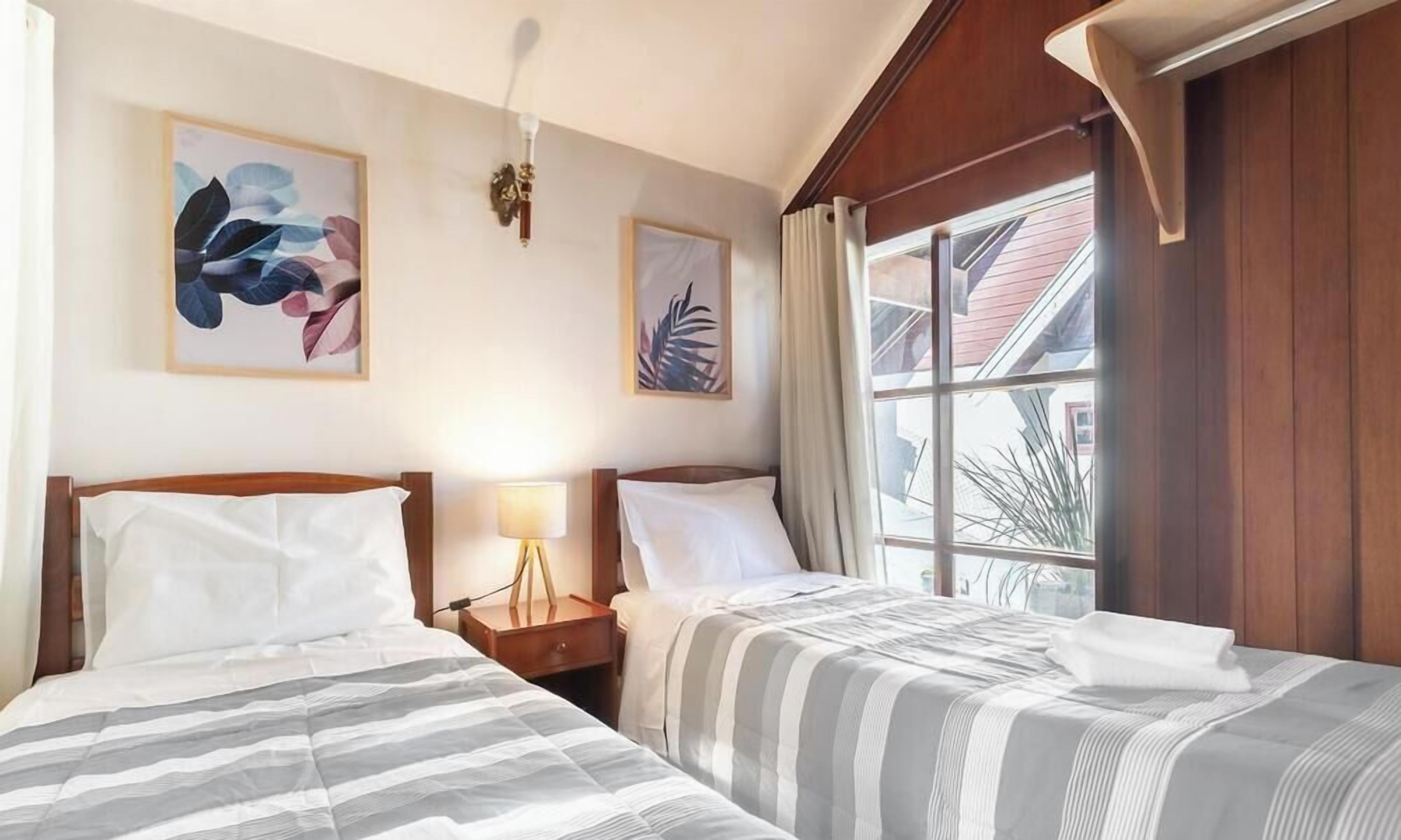 Una habitación de hotel con dos camas, una mesita de noche con lámpara y obras de arte en las paredes.