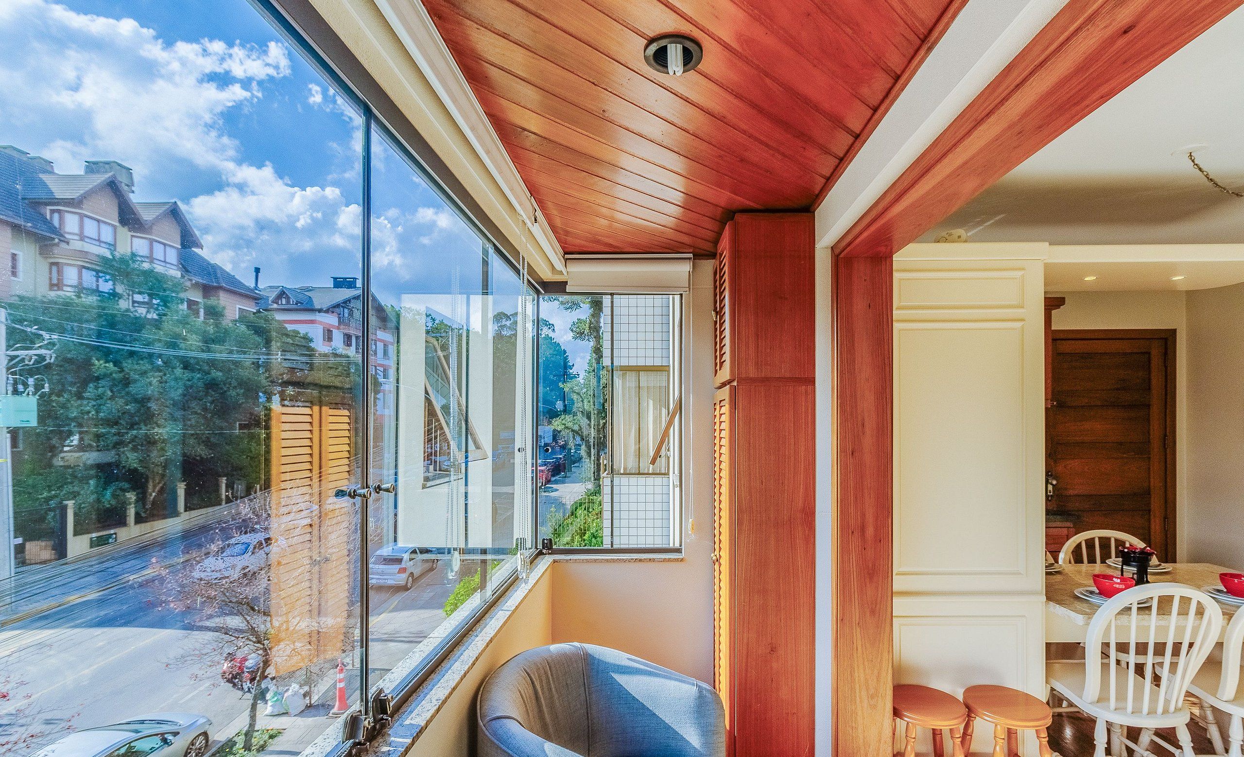 A room with a large window, a wooden ceiling, and a dining area with chairs and a table.