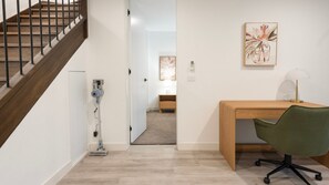 A room with a wooden desk, a green chair, a wooden staircase, and a hallway leading to another room. - The Treetop Townhouse in Templestowe (Templestowe Lower)