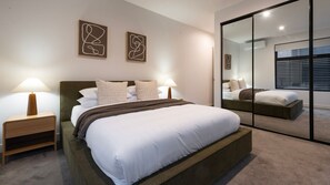 A modern bedroom with a large bed, two bedside tables, a mirror, and abstract wall art. - The Treetop Townhouse in Templestowe (Templestowe Lower)
