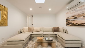 A modern living room with a sectional sofa, a glass coffee table, and a painting on the wall. - The Treetop Townhouse in Templestowe (Templestowe Lower)